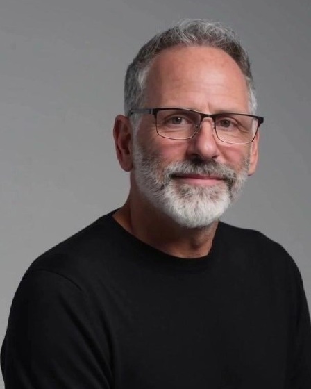 Marc Adam Kravitz wearing glasses and a black shirt against a gray background